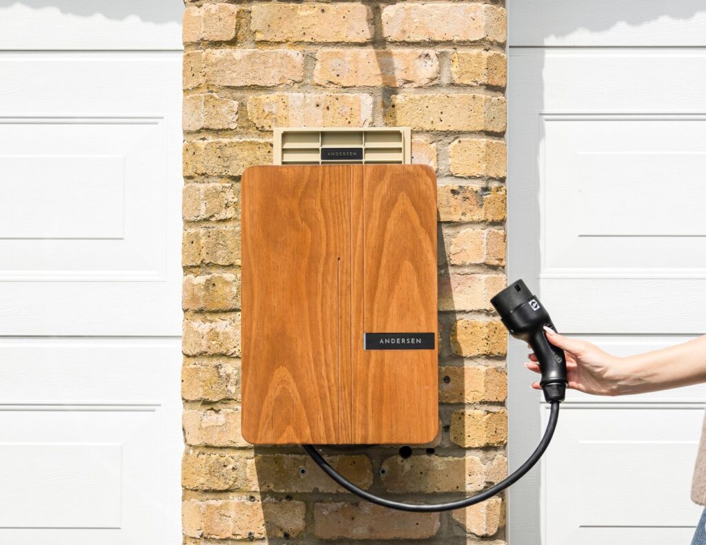 A woman uses a home electric vehicle charger mounted on a brick wall.