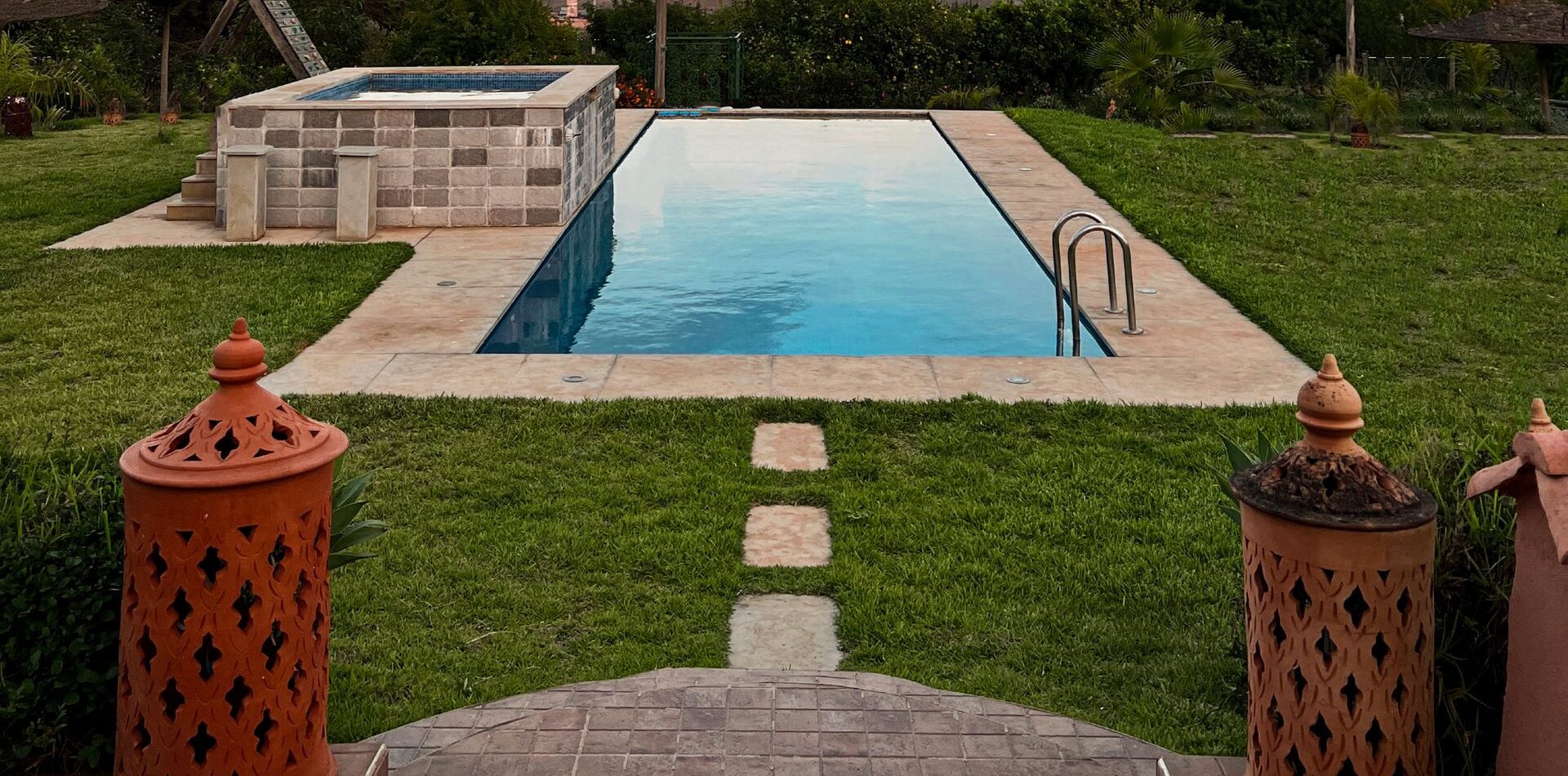 Luxury swimming pool with lush garden view and expansive sky, perfect for relaxation.